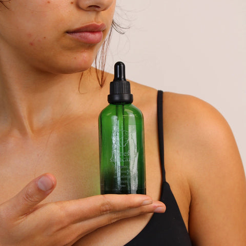 Honest Skincare Organic Rosemary Revitalising Hair Serum 100ml lifestyle shot of a person holding up the green dropper bottle at their chest