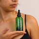 Honest Skincare Organic Rosemary Revitalising Hair Serum 100ml lifestyle shot of a person holding up the green dropper bottle at their chest