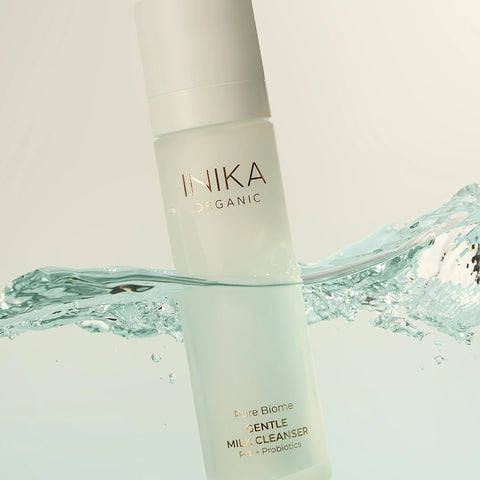 INIKA Organic Pure Biome Gentle Milk Cleanser 100ml lifestyle shot of the bottle partly in clear water with a splash, styled lifestyle photo