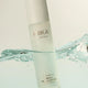 INIKA Organic Pure Biome Gentle Milk Cleanser 100ml lifestyle shot of the bottle partly in clear water with a splash, styled lifestyle photo