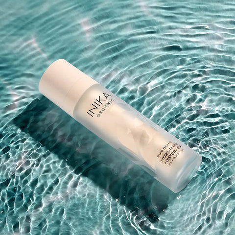 INIKA Organic Pure Biome Hydro-Fluid Moisturiser 50ml lifestyle shot of the bottle lying in clear teal water with ripples, styled lifestyle photo