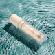INIKA Organic Pure Biome Hydro-Fluid Moisturiser 50ml lifestyle shot of the bottle lying in clear teal water with ripples, styled lifestyle photo