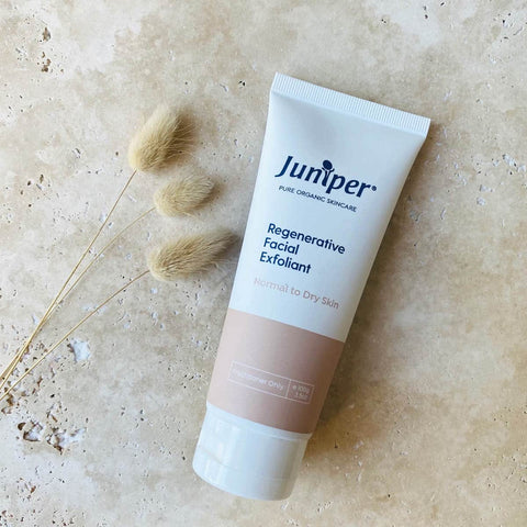 Tube of Juniper Regenerative Facial Exfoliant on a beige background with a dried plant. 