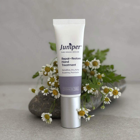 Tube of Juniper Repair + Restore Hand Treatment with flowers in the background.