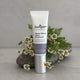Tube of Juniper Repair + Restore Hand Treatment with flowers in the background.