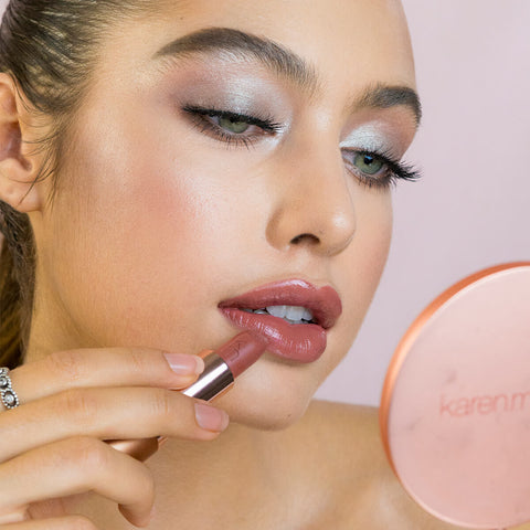 Close-up of a woman applying cordovan natural lipstick, wearing beautiful eye makeup. 