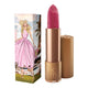 Lipstick next to box packaging that pictures a woman in a pink gingham dress in a city setting. Flower detail on lipstick case lid.