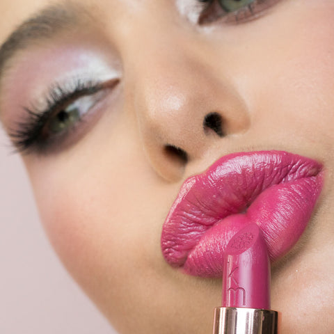 Close-up of a woman applying pink starlet lipstick, wearing beautiful eye makeup. 