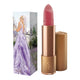 Lipstick next to box packaging that pictures a woman in a sparkling violet dress in front of a castle, in a field of purple flowers. Gold lipstick case with flower detail on lid. Natural, clean cosmetics.