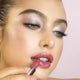 Close-up of a woman applying violet mousse lipstick, wearing beautiful eye makeup. 