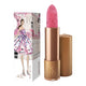 Lipstick next to box packaging that pictures a woman in a glamourous floral dress, in a cityscape. Gold lipstick case with flower detail on lid. Natural, clean cosmetics.