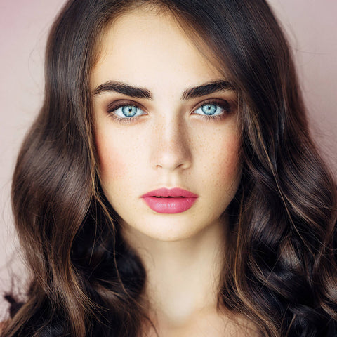 Young woman with light freckly skin tone, blue eyes & brown wavy hair, wearing carnation mist lipstick.