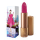 Lipstick next to box packaging that pictures a woman in a glamorous pink dress in front of a cityscape, pink cocktail in hand. Gold lipstick case with flower detail on lid. Natural, clean cosmetics.