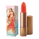 Lipstick next to box packaging that pictures a mermaid in a pearl oyster, with a coral tail. Gold lipstick case with flower detail on lid. Natural, clean cosmetics.