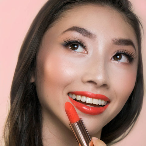 Close-up of a woman holding coral dawn lipstick after applying.