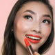 Close-up of a woman holding coral dawn lipstick after applying.