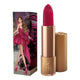 Lipstick next to box packaging that pictures a woman in a magenta dress with giant bow detail in the back and walking past a pink telephone box. Gold lipstick case with flower detail on lid. Natural, clean cosmetics.
