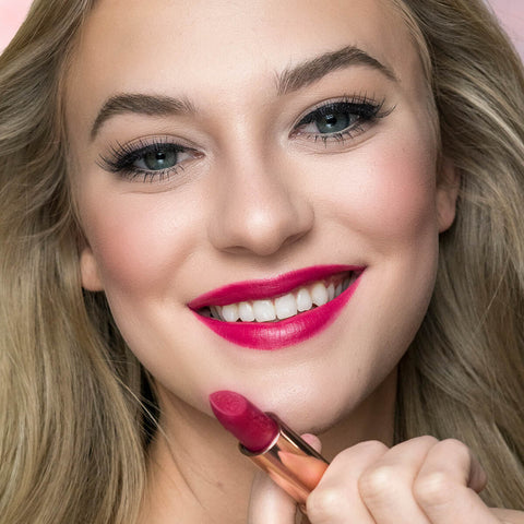 Close-up of a woman holding magenta moon lipstick, after applying.