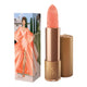 Lipstick next to box packaging that pictures a woman in a peachy dress. Gold lipstick case with flower detail on lid. 