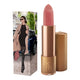 Lipstick next to box packaging that pictures a chic city-slicker in a trench coat. Gold lipstick case with flower detail on lid. 