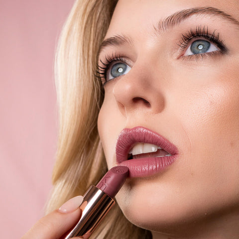 Close-up of a woman applying driven lipstick, wearing natural eye makeup. 