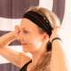 Woman with a black headband adjusting her hair against a blurred background