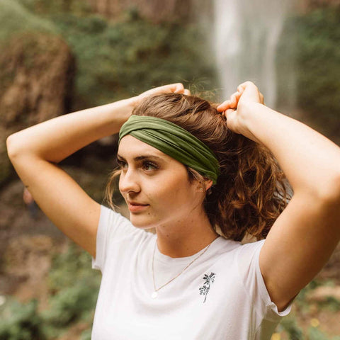 Woman with a green headband adjusting her hair outdoors.