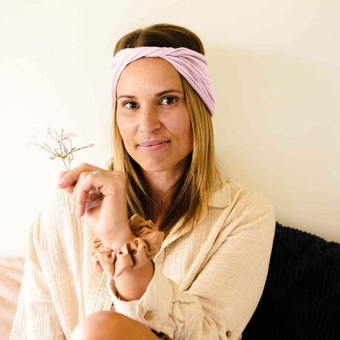 Woman wearing a light pink headband holding a small plant against a white background.
