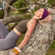 Person laying on a large tree branch in a park wearing athleisure clothing and Kooshoo Twist Headband. 