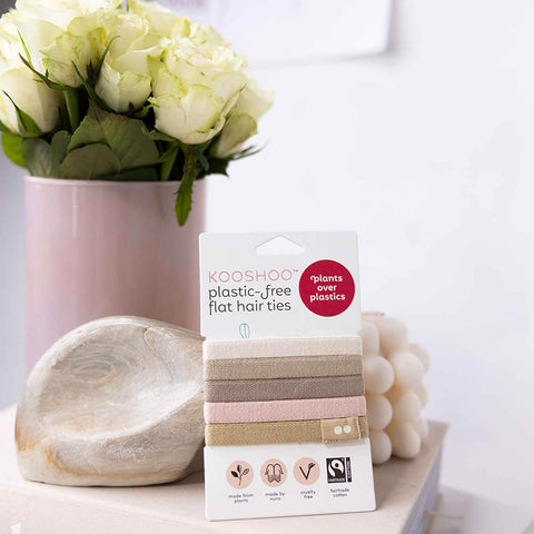 Kooshoot plastic-free flat hair ties packaging on a surface with flowers and decorative items in the background