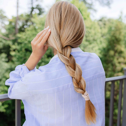 Person with a long braid wearing a light blue shirt outdoors