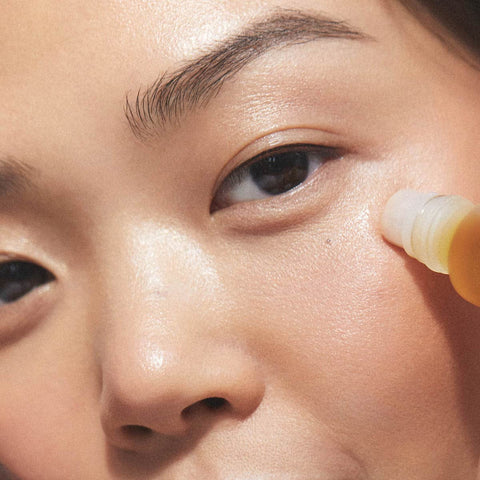 Close-up of a model applying the noni eye oil using the roll-on applicator. 
