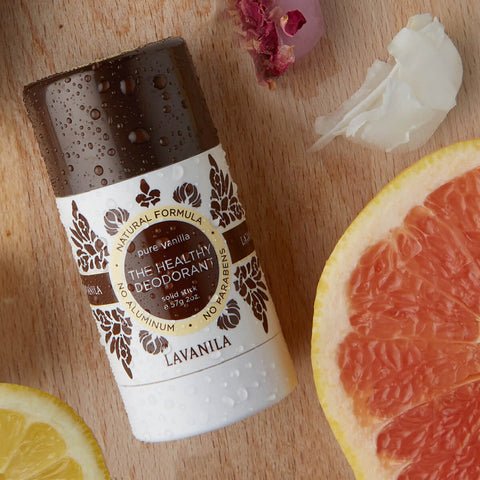 Lavanila The Healthy Deodorant Pure Vanilla lifestyle shot of the stick lying beside grapefruit slices and a white flower on a wooden board