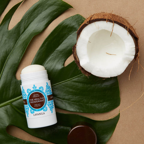 Lavanila The Healthy Deodorant Vanilla Coconut 57g lifestyle shot of the stick lying beside half a coconut and a large green leaf