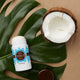 Lavanila The Healthy Deodorant Vanilla Coconut 57g lifestyle shot of the stick lying beside half a coconut and a large green leaf