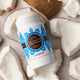 Lavanila The Healthy Deodorant Vanilla Coconut 57g lifestyle shot of the stick resting among broken pieces of white coconut, close up