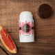 Lavanila The Healthy Deodorant Vanilla Grapefruit 57g lifestyle shot of the stick on dark wood beside half a grapefruit and its cap