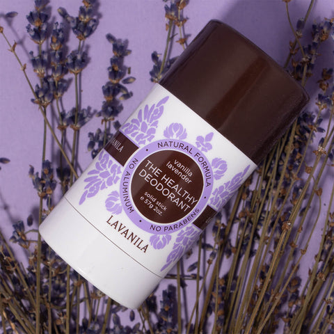 Lavanila The Healthy Deodorant Vanilla Lavender 57g lifestyle shot of the stick lying on dried lavender against a lilac backdrop