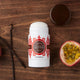 Lavanila The Healthy Deodorant Vanilla Passion Fruit 57g lifestyle shot of the stick beside vanilla pods and a halved passion fruit on dark wood