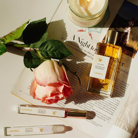 Lavanila The Healthy Fragrance Pure Vanilla 50ml lifestyle flat lay of the bottle with a rose, a roller and a folded newspaper