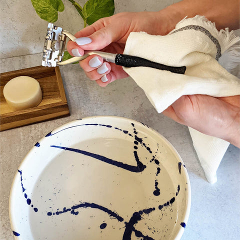 Person cleaning a reusable razor on a bathroom counter