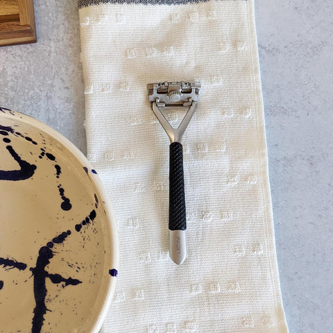 Shaving razor on a textured towel with a ceramic bowl in the background