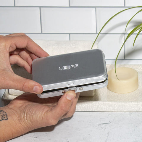 Leaf Shave Single Edge Travel Case lifestyle shot of two hands holding the closed metal case above a bathroom counter, styled lifestyle photo