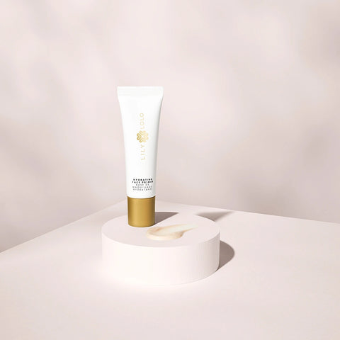 Lily Lolo Hydrating Face Primer 25ml lifestyle shot of the white and gold tube on a white round plinth against a pale backdrop