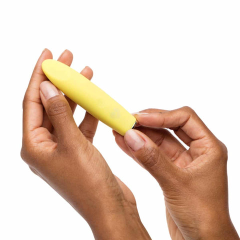 Yellow bullet massager held by two hands against a white background.