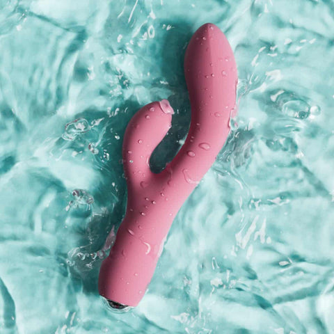 Pink sex toy partially submerged in water with a light blue background.