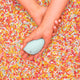 Hand holding a small blue personal massager on a background of colourful sprinkles.