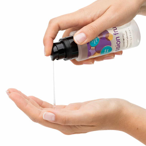 Person holding a bottle of passionfruit lubricant and pumping into another hand against a white background.