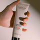 Hand holding a tube of Mádara Intense Repair Body Cream against a neutral background.
