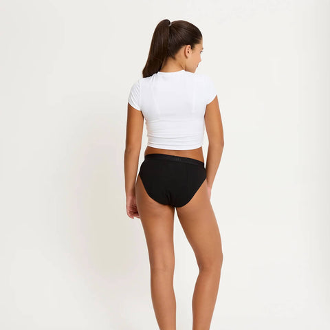 Model wearing Modibodi Teen Hipster Bikini Moderate-Heavy in black, back view of period underwear.